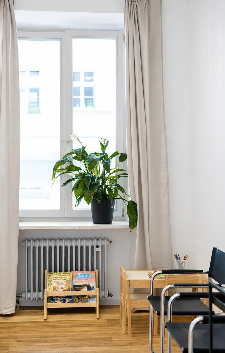 Wartebereich mit hohem Fenster, Pflanze, Kinderbüchern und Maltisch