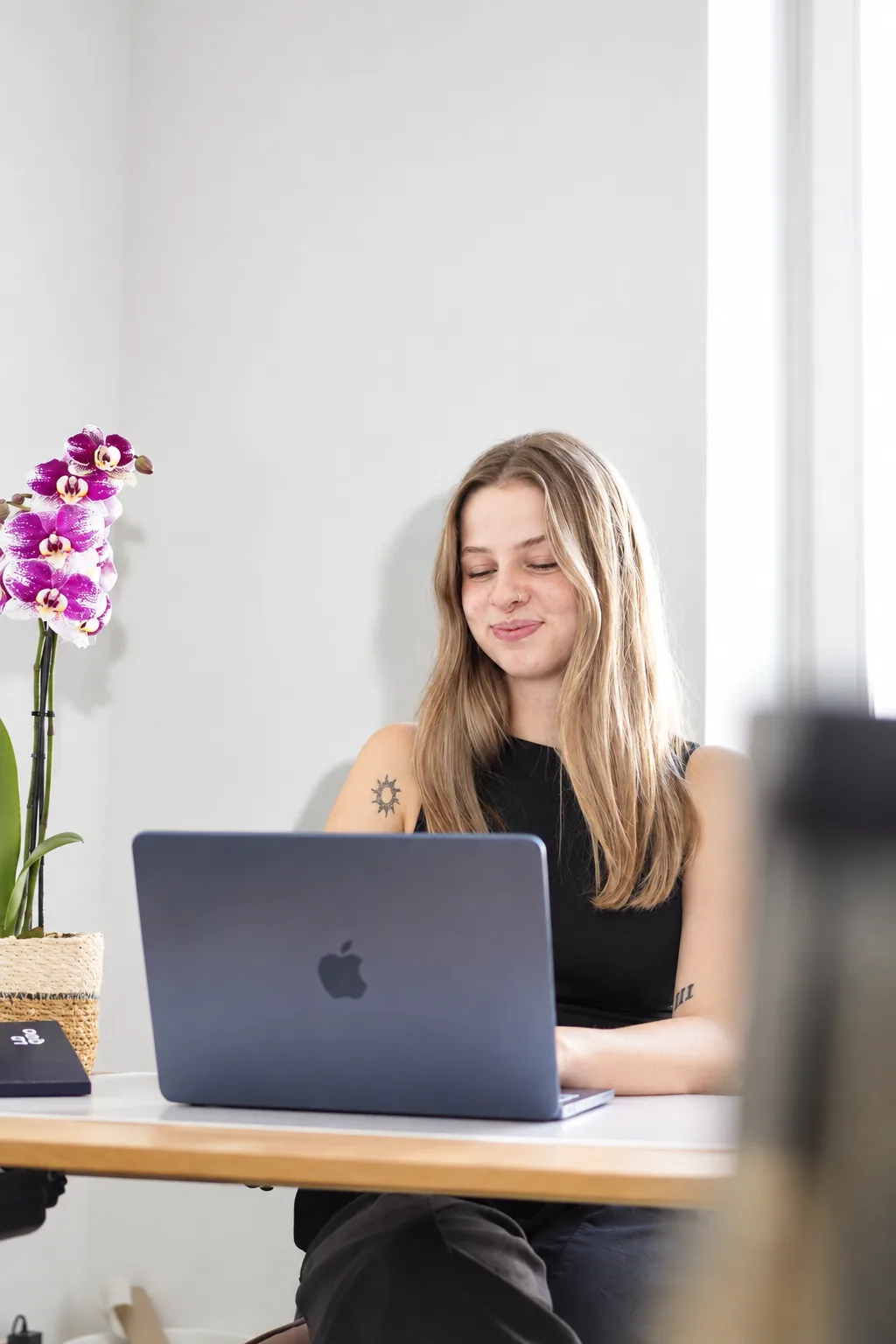 Julia arbeitet lächelnd am Laptop, daneben eine Orchidee
