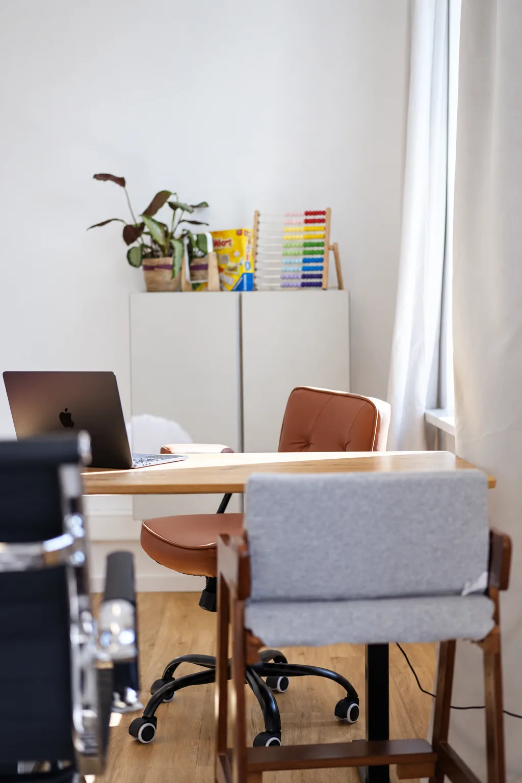 Behandlungszimmer mit Holztisch, Laptop und Therapiematerial auf dem Schrank